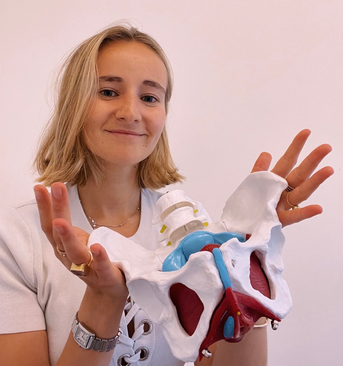 Eléonore Boonen souriante, tenant un modèle anatomique du bassin dans ses mains